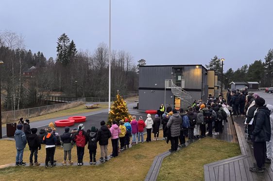 Elever og ansatte står samlet i amfiet rundt nytent juletre