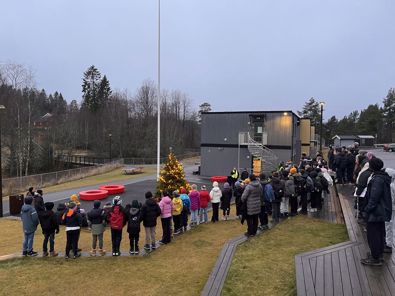 Elever og ansatte står samlet i amfiet rundt nytent juletre