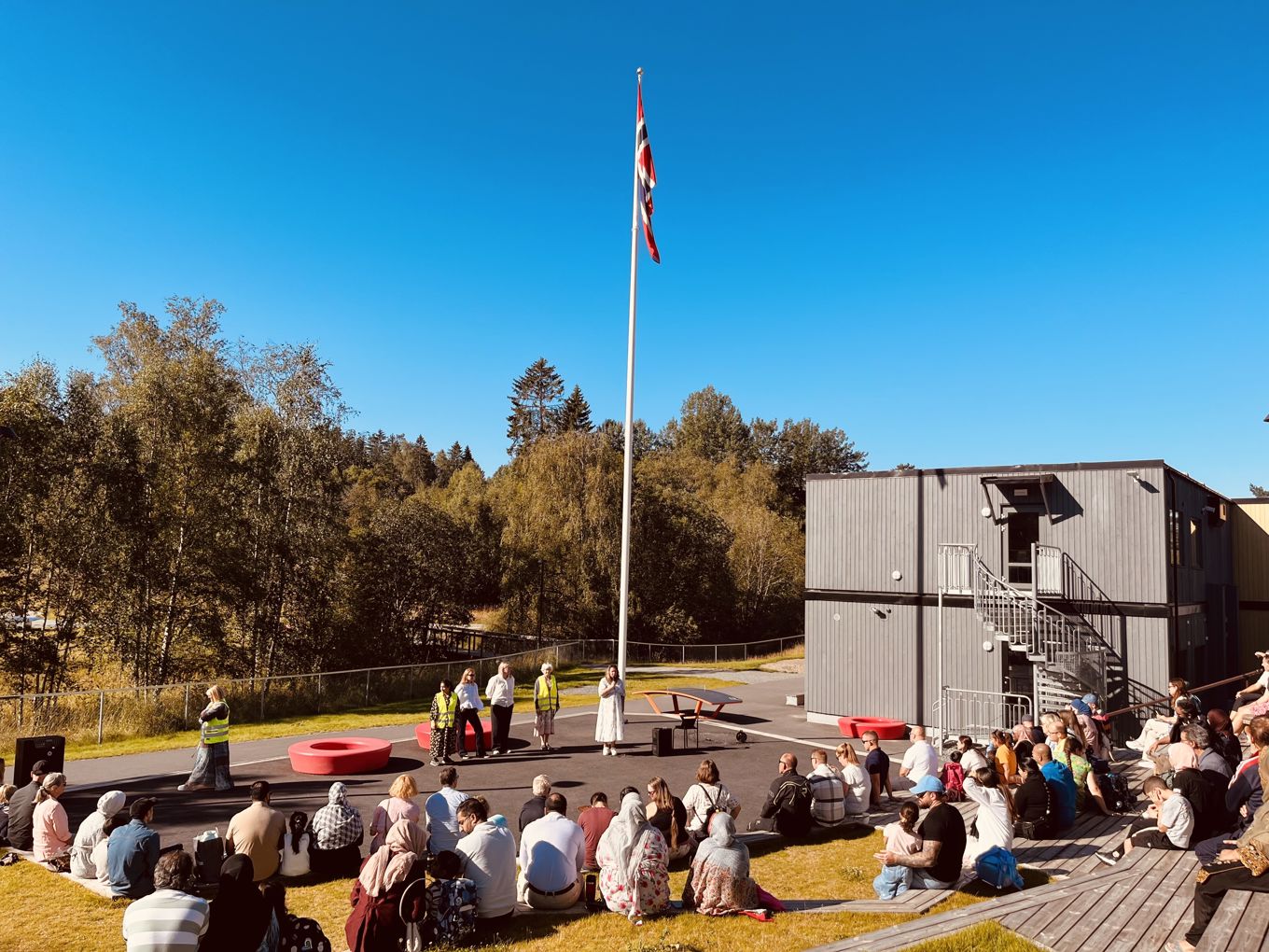 Foresatte og skolestartere som sitter på amfiet foran en flaggstang